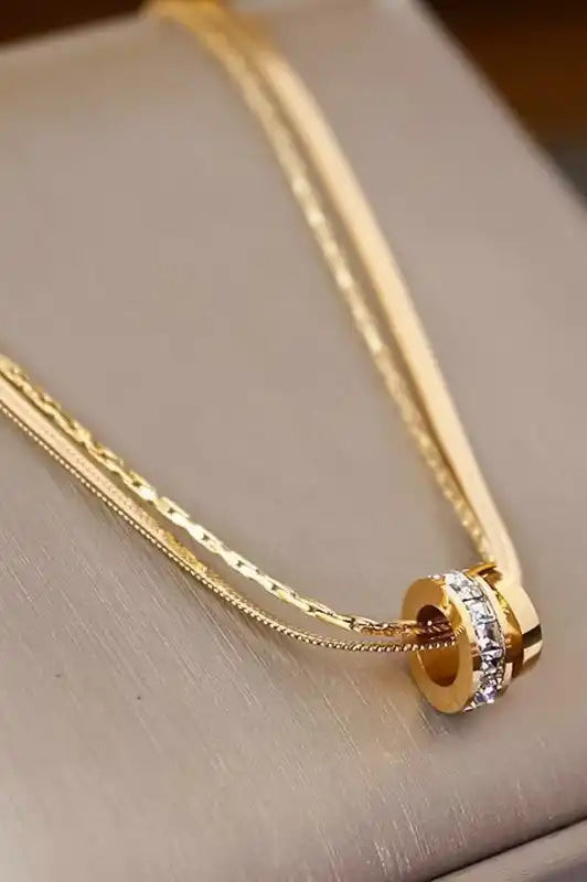 Gold-toned layered necklace with crystal-studded ring pendant.