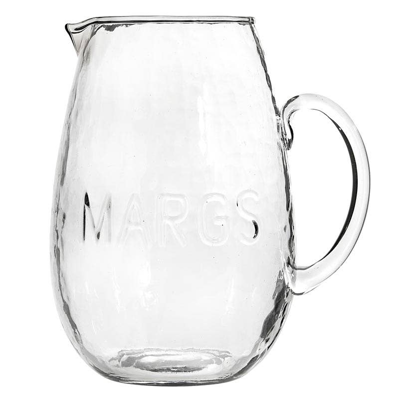 Clear hammered glass pitcher embossed with “MARGS” and curved handle — handcrafted drinkware from The Pink Doxie Boutique.